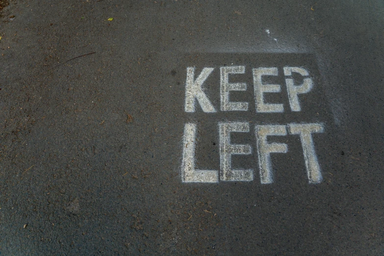 a white chalk written keep left on a black pavement