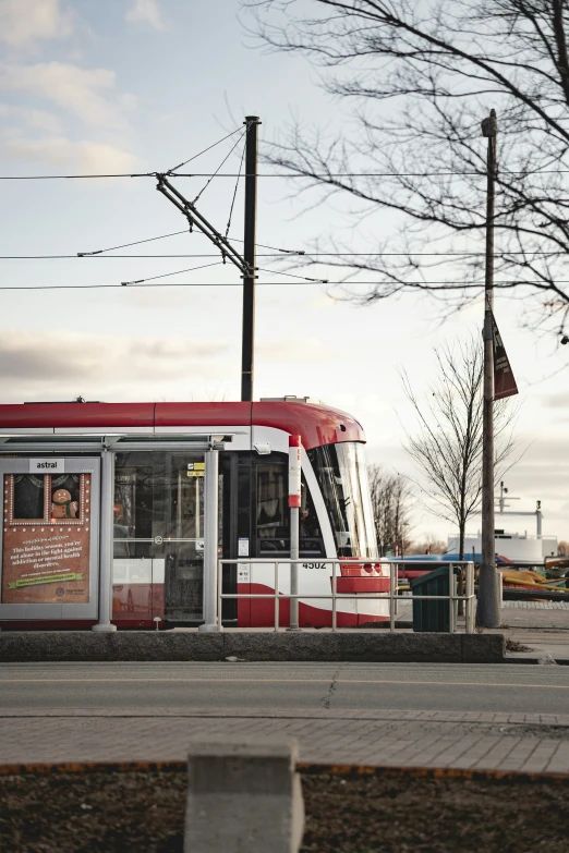 a red and white trolley car pulling up to the side of a road