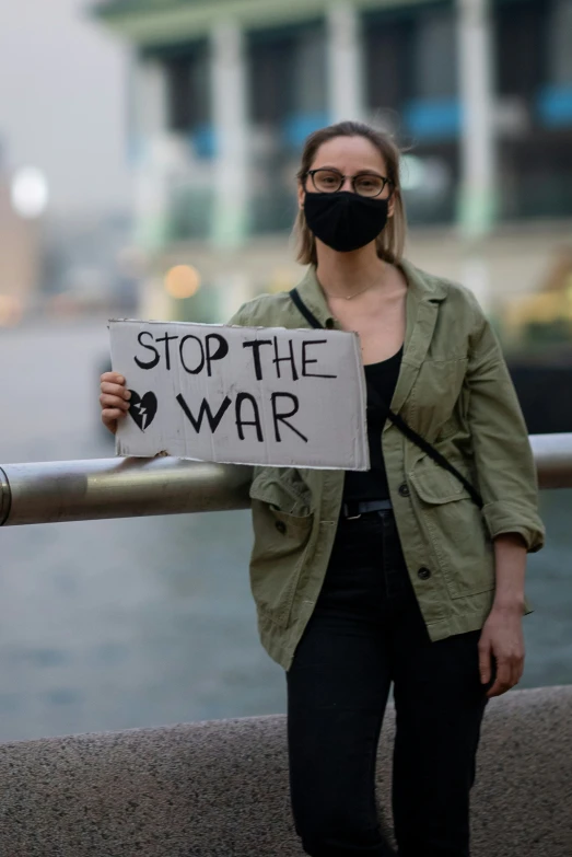 a woman wearing a mask holds a sign while holding a barricade behind her