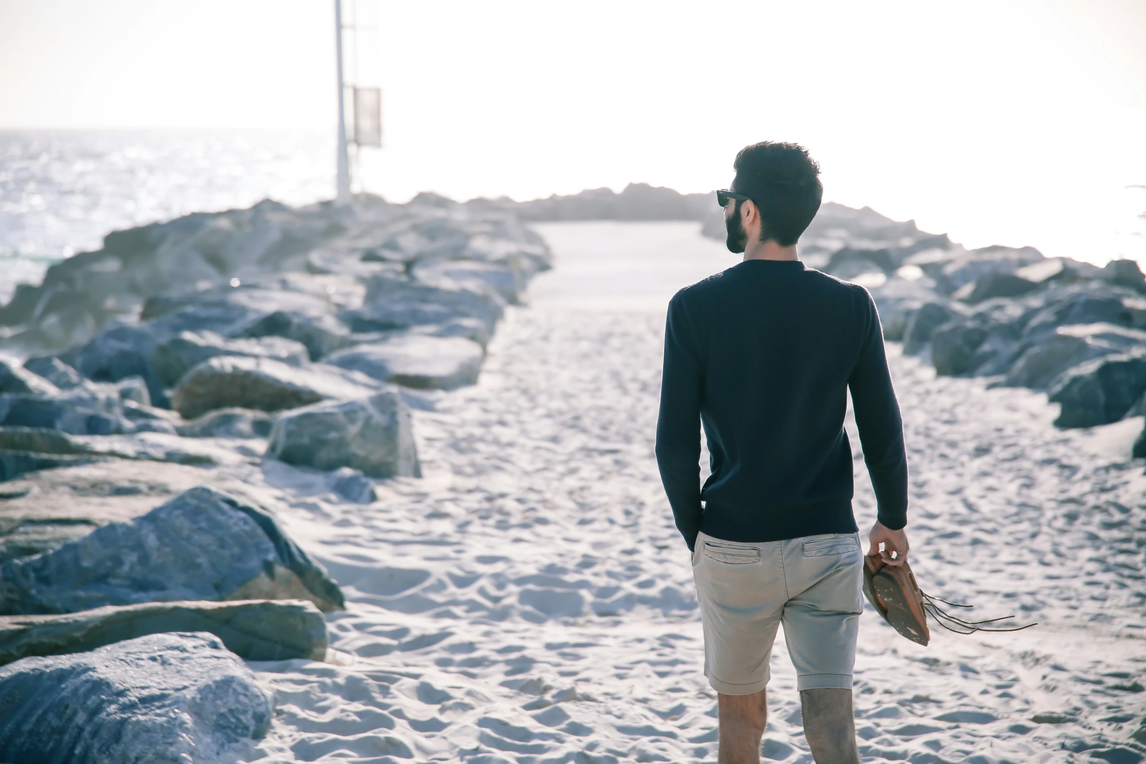 there is a man walking on the beach with a hat and gloves