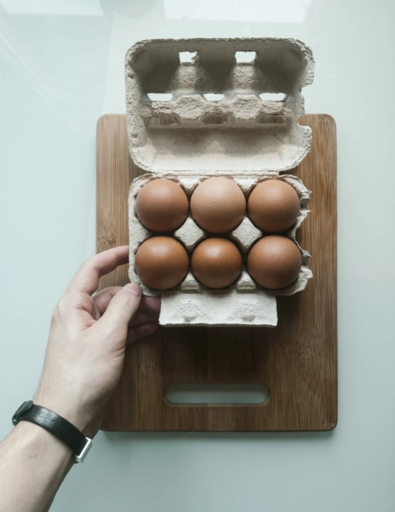 a person placing egg in an egg carton on top of a wooden surface