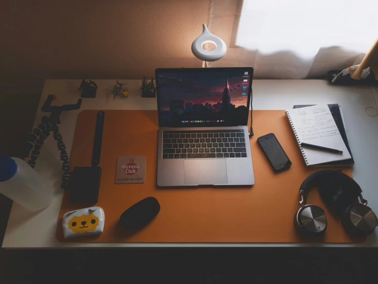 a laptop, headphones, notebook and a phone on a desk