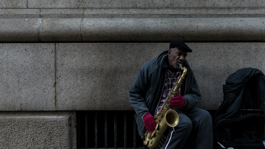 a man sitting on the curb playing a saxophone
