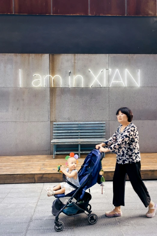 a woman and baby in a stroller walking next to a building