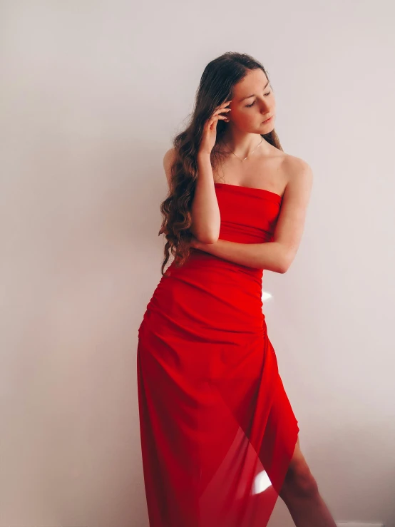 a woman in a red dress is leaning on the wall