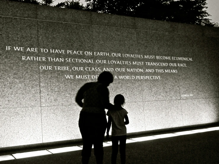 a woman and girl standing in front of a wall that reads, we are to have peace on earth