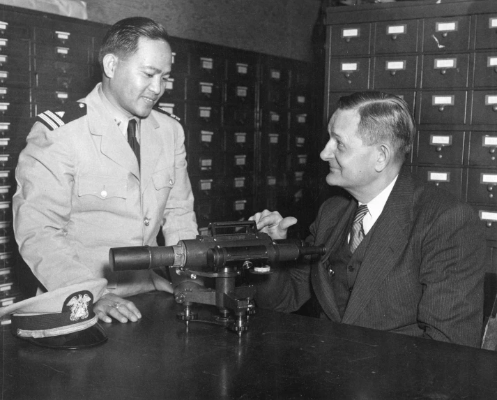 two men in suits standing around a table with a telescope