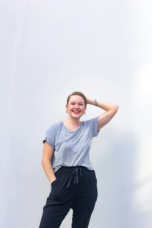 a young woman standing in front of a white wall wearing a gray shirt