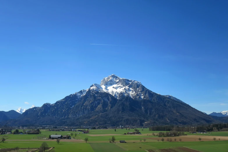 the top of a snowy mountain surrounded by green fields