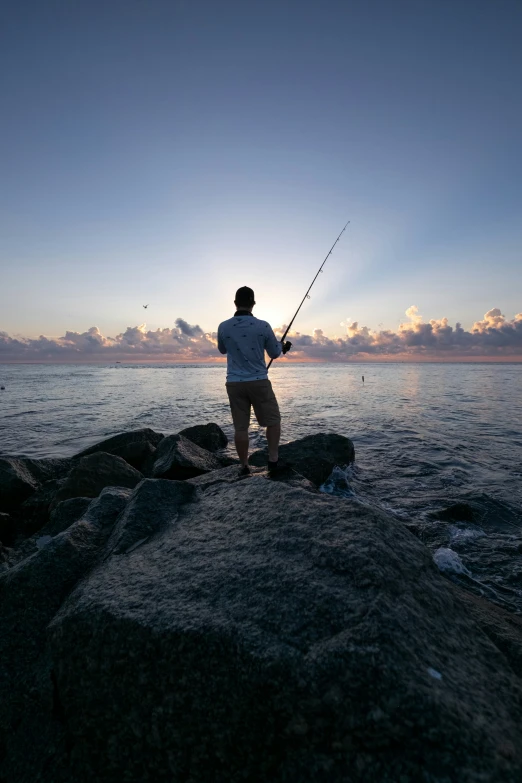 a man stands on rocks while fishing at the ocean