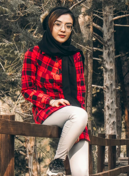 a girl with glasses is sitting on a wood fence