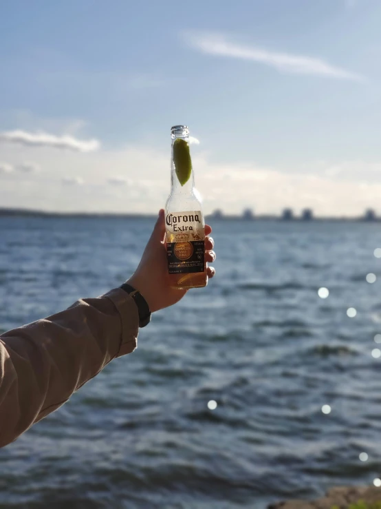 someone holding a bottle in their hand by the water