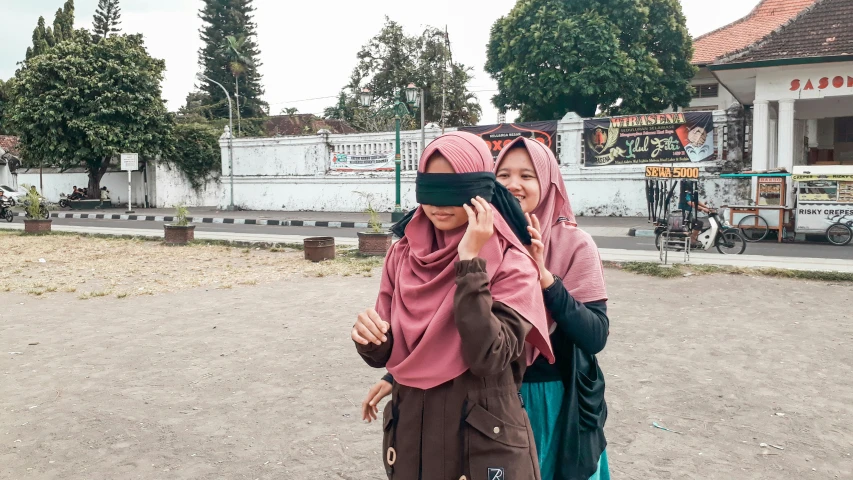 two women walk down the street with blindfolds