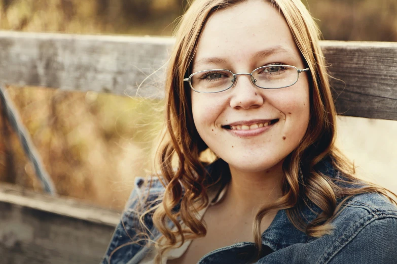 a woman wearing glasses smiling on a bench