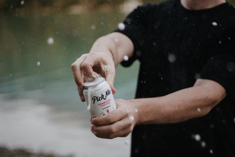 person holding up an energy drink in front of water