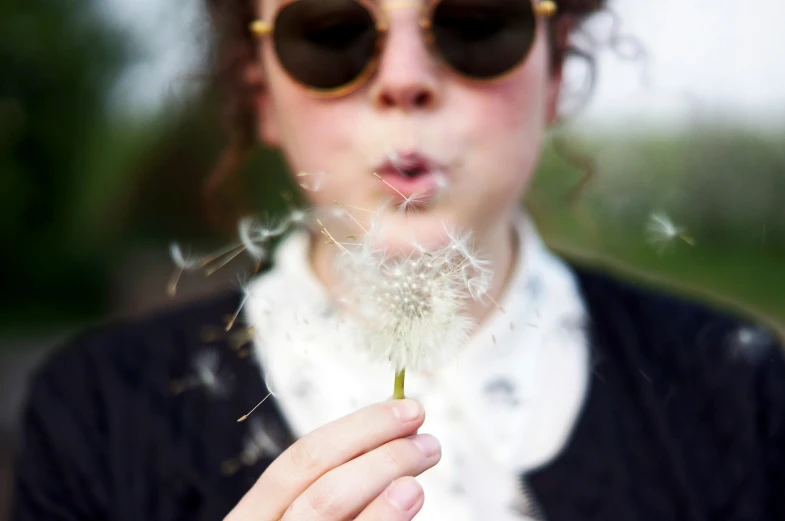 there is a woman holding a dandelion blowing