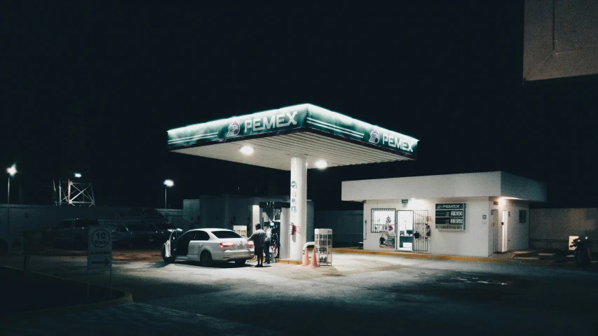 a lit gas station in the dark with a few people filling their cars