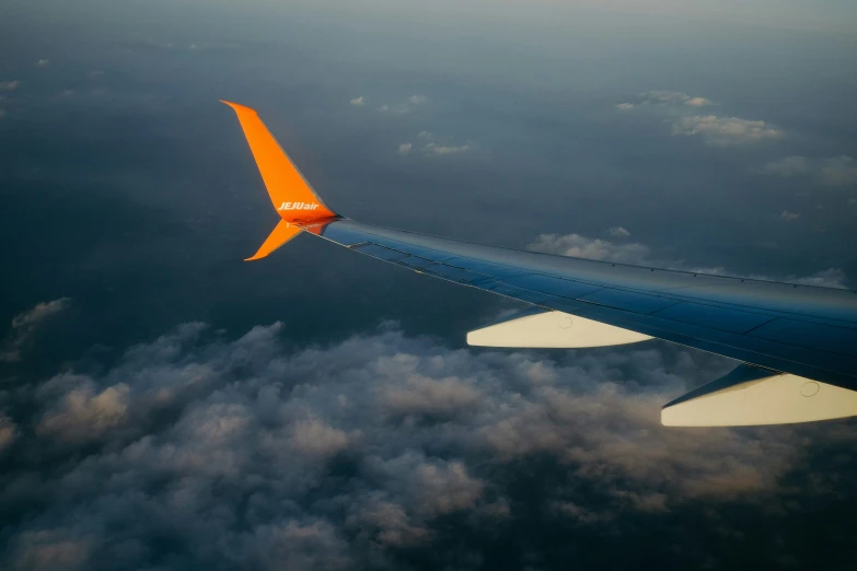 a plane wing with some clouds in the background