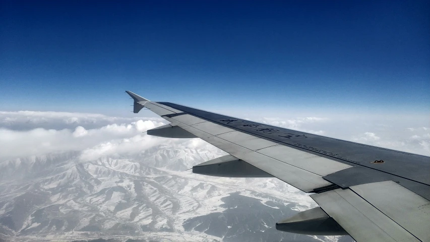 a view from a airplane of the wing and the ground with mountains in the background