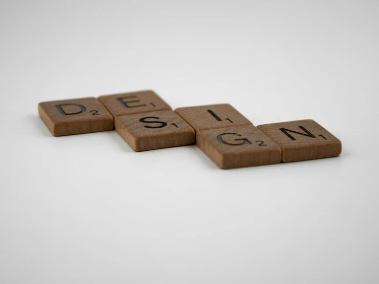 two letters made of brown scrabble tiles spelling out the words genius and genius