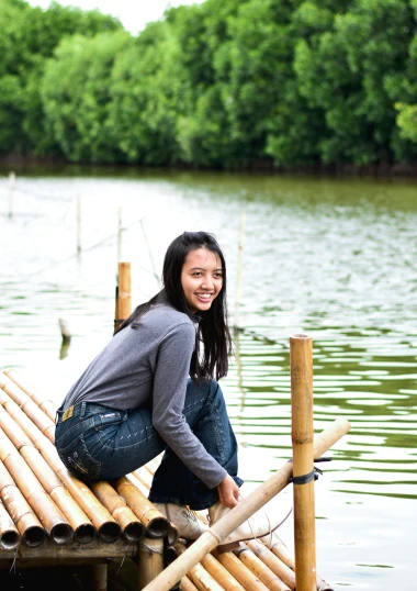 a girl sitting on bamboo raft by water