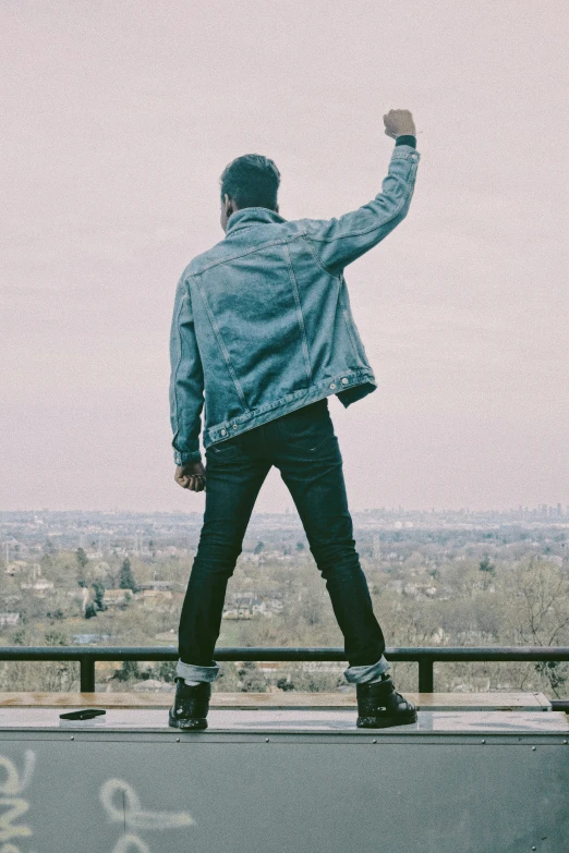 a man in blue jacket standing on a ledge raising his fist