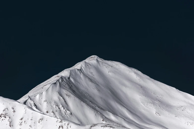 the peak is covered in snow as a clear blue sky shines on