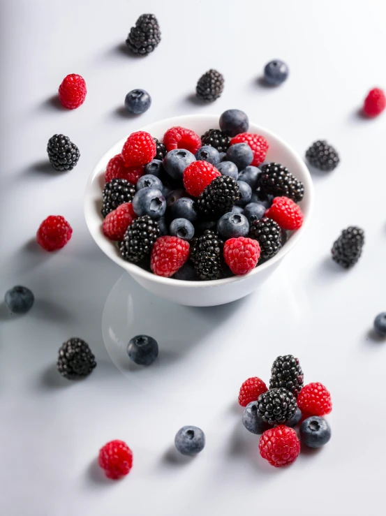a bowl of fresh berries and other berries on a white table