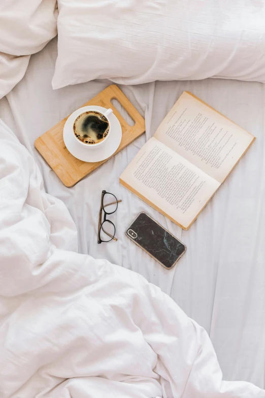 a coffee cup and a book are on a bed