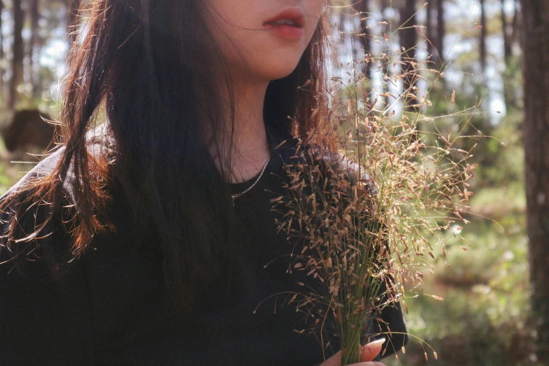 a woman holds wild grass in the woods