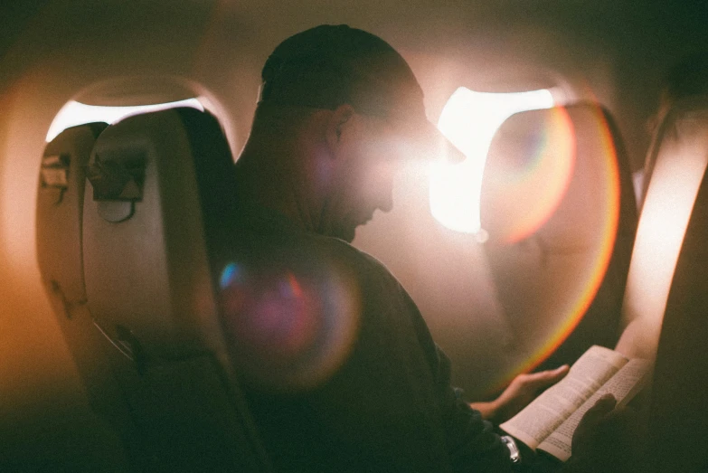 man reading a book on a plane, in a dark airplane