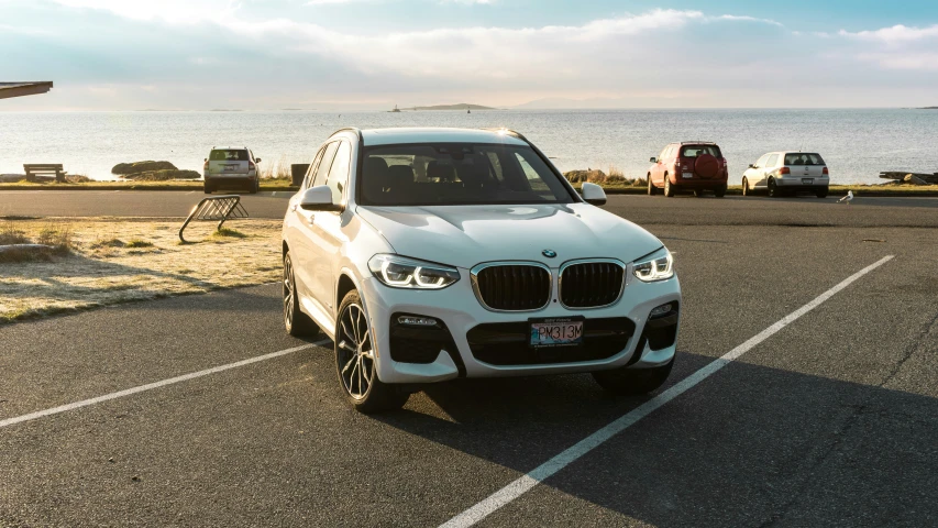 the front of a white bmw suv parked by the water