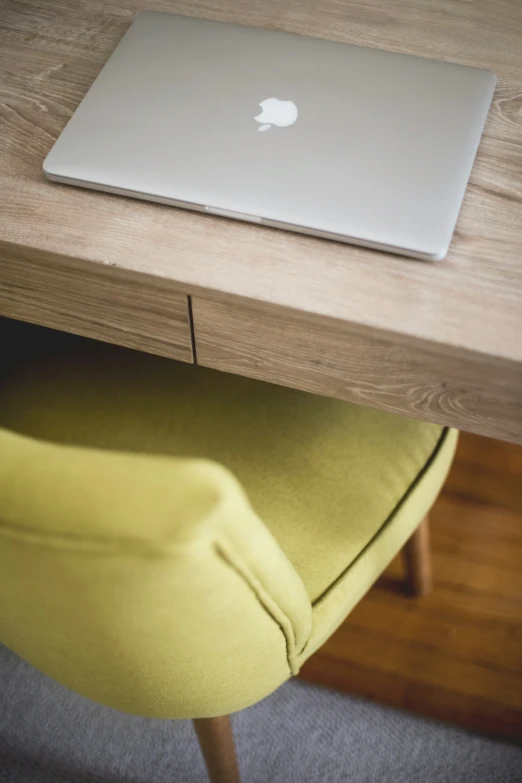 an apple laptop on a wooden table next to a yellow chair