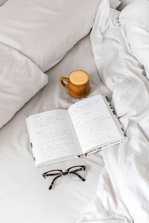 an open book, glasses and a gold ring on top of a white bed