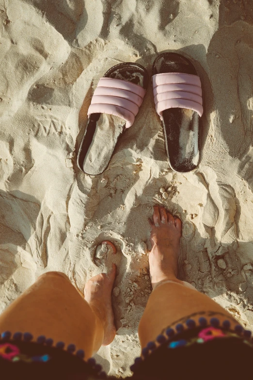 person's feet and sandals on sand near the ocean