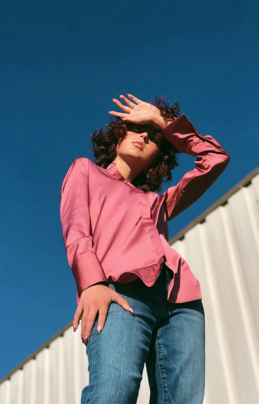 a woman wearing a pink top stands against a building