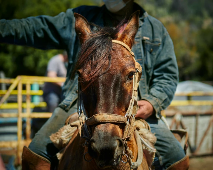 cowboy riding horse in corral area while another man is behind him