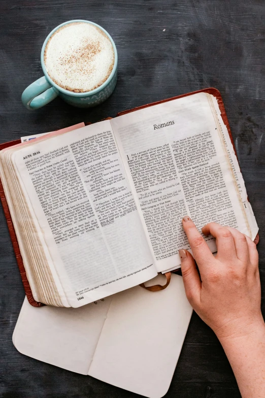 a person reading a book next to a cup of coffee