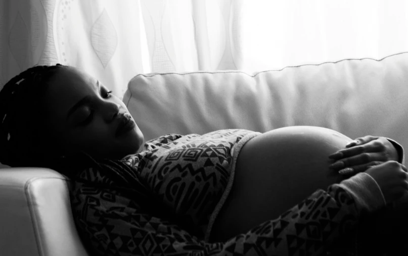 a pregnant lady asleep on the back of a sofa