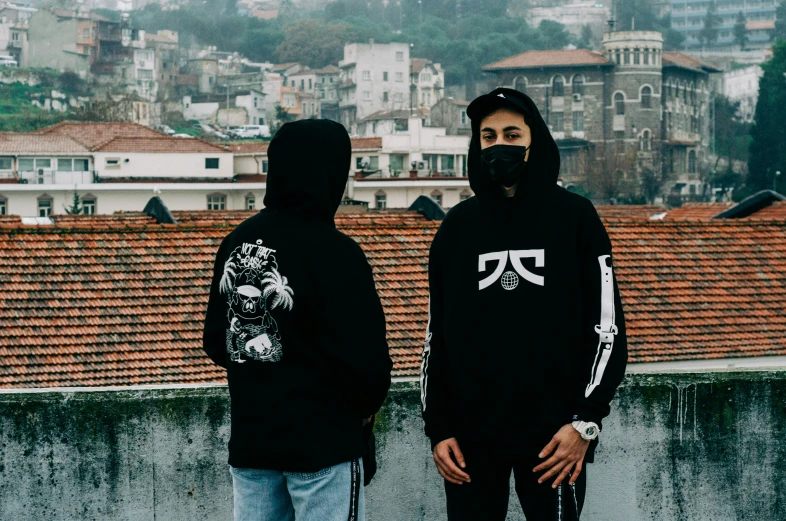 two men standing on a wall wearing hoodies and helmets