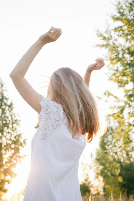 a woman stands in the grass with her arms in the air