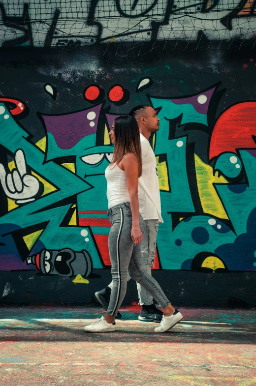 a woman and a man walking along side a graffiti wall