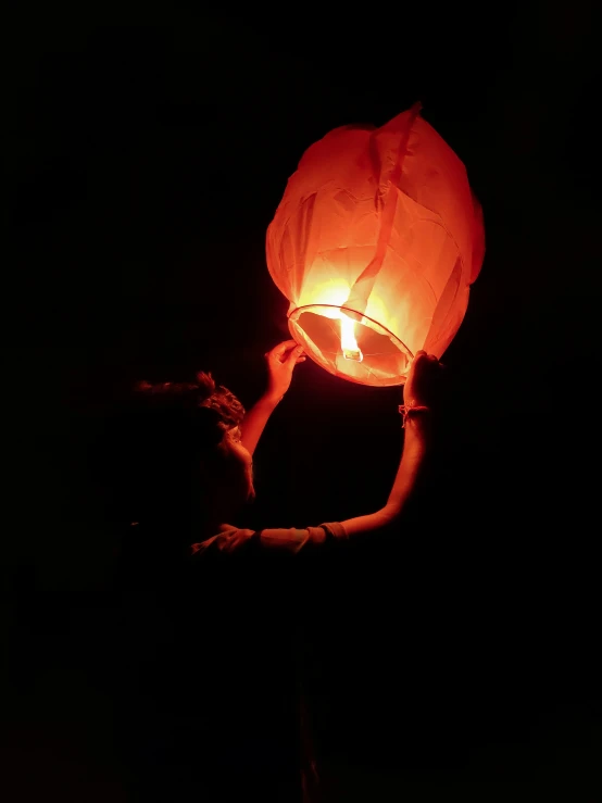the person is holding an illuminated paper lantern in their hands