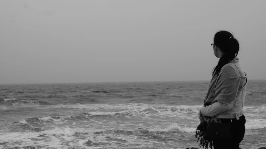 a woman stands on a rock and stares out into the ocean