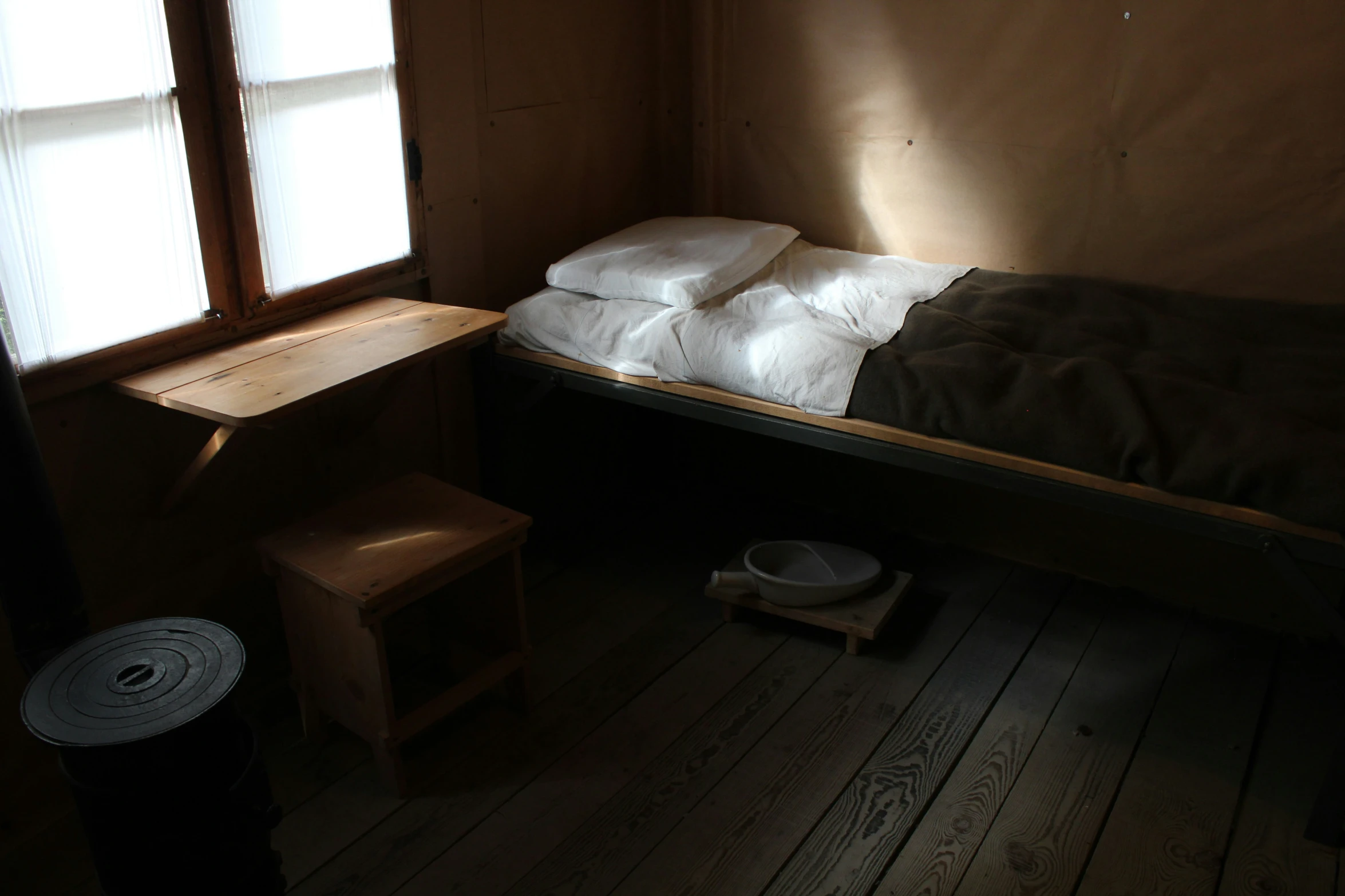 a bare bedroom with bed, window and stool