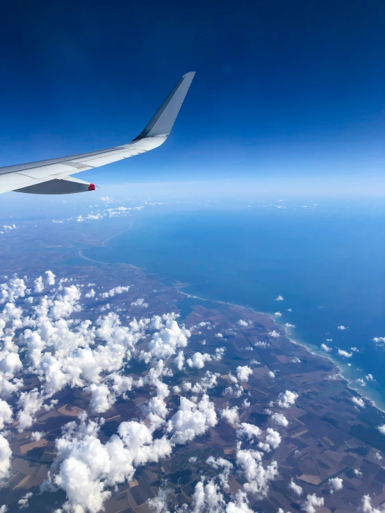 an airplane's wing in the sky looking down on some white clouds and blue water