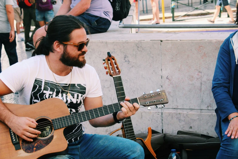 a man holding an acoustic guitar on the side of the road