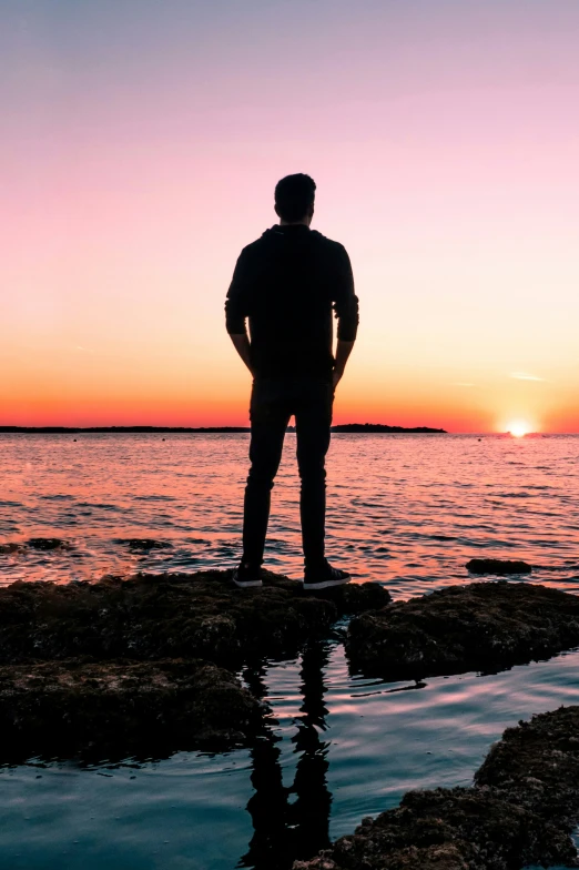 the man standing on the rocks is looking at the sunset