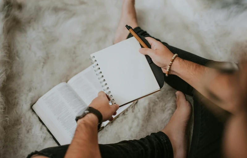 someone holding an open book and writing in a notebook