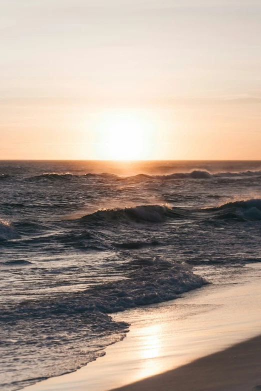 the sun is setting at the beach and some waves are crashing